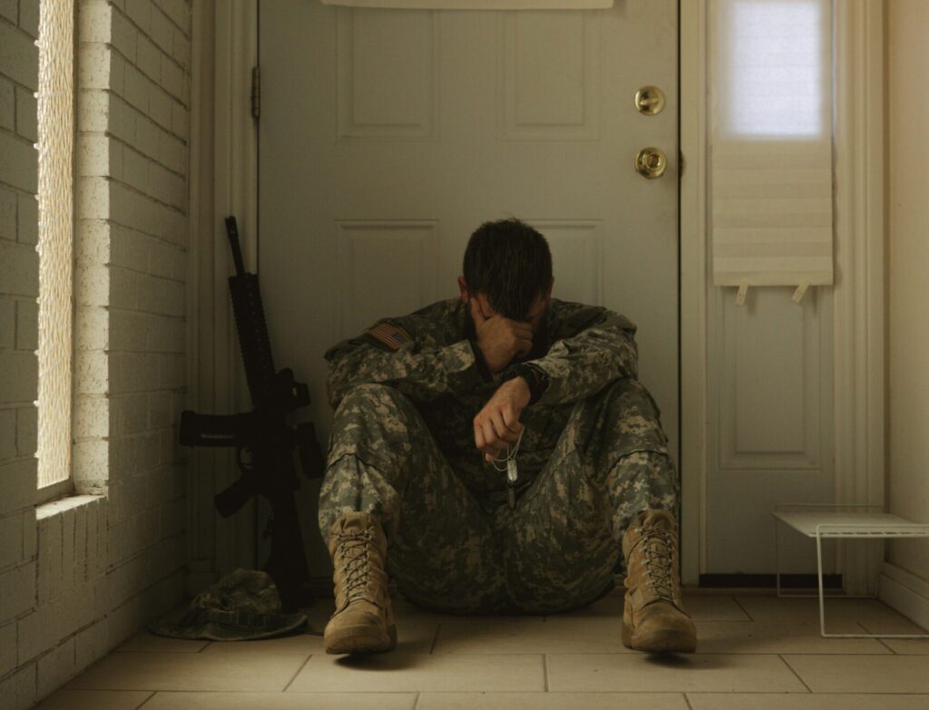 overwhelmed veteran with head in hands sitting outside his front door